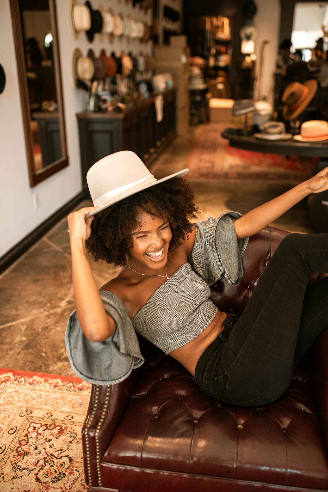 African American woman sitting happily in a stylish boutique, trying on hats and having fun.