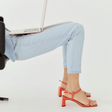 Woman in denim and heels using a laptop while reclining, showcasing a modern lifestyle.