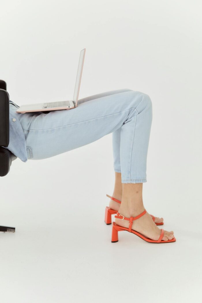 Woman in denim and heels using a laptop while reclining, showcasing a modern lifestyle.